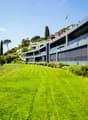 modern apartment complex on hillside, large green lawn, fenced area, glass balconies