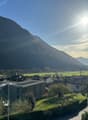 House exterior, large windows, flat roof, modern architecture, solar panels, surrounded by green grass, view of a valley, mountains in the background