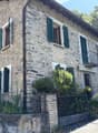 2-story stone house with green shutters, balcony, and landscaped garden in front