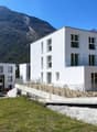 Modern white building, 4 stories, glass windows, metal railings, surrounded by mountains and greenery