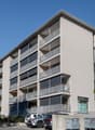 Modern apartment building, grey walls, multiple balconies, ground floor commercial space