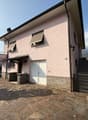 Two story house, pink exterior, white door, garage, stone walls, stairs, windows with awnings, outdoor patio