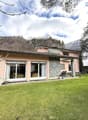 Detached house, pink exterior, large windows, spacious lawn, exterior AC unit, patio with chairs, trees, bushes, mountain in the background