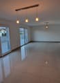 Spacious open-plan living area with large windows, hardwood floors, and modern pendant lighting fixtures. The room has a clean, minimalist design with a neutral color palette.