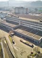 Large multi-story industrial building with a flat roof, surrounded by other commercial and industrial buildings. The building has a rectangular shape and appears to be used for manufacturing or warehousing purposes. There are several vehicles parked in th