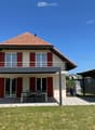 2 story house, red tiled roof, white walls, red shutters, covered balcony, outdoor dining table