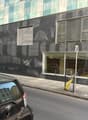Modern building with glass facade, multiple windows, black exterior, glass door, trash bin, parked car