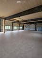 Empty room with concrete floor, wooden ceiling, large windows, and metal beams.
