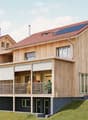 wooden house, modern design, balcony, solar panels on the roof, chimneys, open grassy area in front