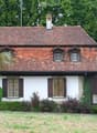 2 story house, brown roof, white walls, large chimney, multiple windows, surrounded by greenery and grass
