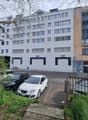 white 3 story building, windows, trees, sidewalk, cars parked, people walking, bicycles