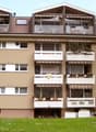 6 stories apartment building, brown color, multiple balconies, grass, tree, street