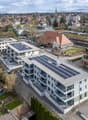 Multiple residential buildings, solar panels on rooftops, parking lot, street with traffic