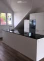 modern kitchen with island, black countertops, stainless steel sink, wooden floors, white cabinets, large windows