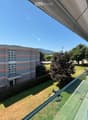 Apartment building, balcony with glass railing, landscaped garden, tree, lawn, distant mountain view