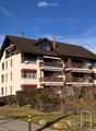 A two-story residential house with a brown tiled roof, multiple windows, balconies, and a well-maintained garden area.