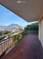 Balcony with tiled floor, black railings, overlooking a road and a lake