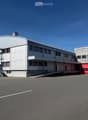 Large industrial building with white walls, red doors, and a large parking area in front