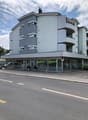 4 story building, gray exterior, glass windows, balcony, glass doors, plants, cars parked