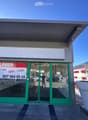 Commercial building with glass doors and windows, green frame, signboard, and a large white planter