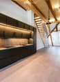 Modern kitchen with black cabinets, stainless steel appliances, and a sleek design, featuring a staircase leading to an open loft area.