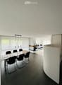 Dining room with a long wooden table, black chairs, white walls, white ceiling, fireplace, white curtains, and a white curved wall.