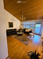 living room with wooden floor, chandelier, black leather couches, coffee table, rug, picture frame, lamp, ottoman, potted plant, balcony