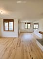 Empty room with hardwood floors, white walls, large windows, and a fireplace with a stone mantle.