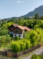 detached house with tiled roof, surrounded by green trees, situated in a scenic area with mountains