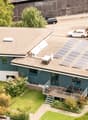 Blue house with solar panels on the roof, wooden deck with outdoor seating, multiple cars parked in the parking lot