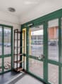 Entrance hall with green glass walls, tiled floor, small shelf, and a view of the street outside