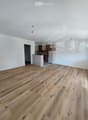 empty room, wooden floor, white walls, open door, kitchen area, cabinets, countertop, ceiling lights