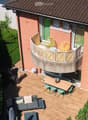 Wooden deck area with a sofa, coffee table, dining table, chairs, and a small balcony with additional seating.