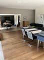 Living room with hardwood flooring, a sofa, coffee table, and a dining area with a table and chairs visible in the background.