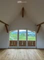 Empty room with wooden floor, white walls, and large glass doors with wooden frames. View of a green field and mountains.
