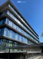 Modern multi-story building with large glass windows and a sleek, contemporary design. The structure features clean lines and a combination of glass and concrete materials.