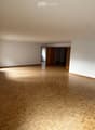 Empty room with wooden herringbone flooring, white walls, and large windows. No furniture or equipment visible.