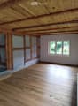 Unfurnished Room. Empty room with wooden ceiling, wooden flooring, and white walls. Two windows with wooden frames and a power outlet on the wall.