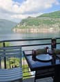 Balcony / Terrace. Balcony with a scenic lake view, featuring a table with chairs, a bottle, bread, and a cup.