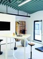 Furnished Room. Modern office space with white tables, laptop, stools, a large screen, a ball chair, and a treadmill.