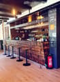 Wooden bar counter with hanging wine glasses, bottles, and stools, illuminated by hanging lamps.