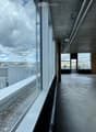 Modern balcony with large glass windows, concrete floor, and a view of the cityscape and surrounding buildings.