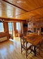 Cozy wooden-paneled room with a dining area, sofa, and cabinetry, featuring large windows and a chandelier.