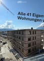 A modern multi-story building under construction with scaffolding, cranes, and a clear blue sky in the background.