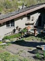 A rustic garden area with a small house, potted plants, outdoor furniture, and a stone pathway.