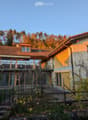 3 story house, yellow exterior, red tiles, large balcony, garden, forest backdrop
