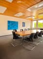 Conference room with a long wooden table surrounded by black chairs, a sculpture on a side table, and artwork on the walls. Large windows provide natural light.