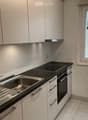 Modern kitchen with white cabinets, stainless steel sink, oven, and a window offering a view of the surrounding area.