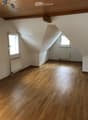 Empty attic room with wooden flooring, white walls, and two windows with slanted ceilings.