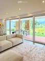 Living Room. Modern living room with large sliding glass doors opening to a patio, a sectional sofa, ottoman, coffee table, floor lamp, side table, and dining area with chairs and a table.